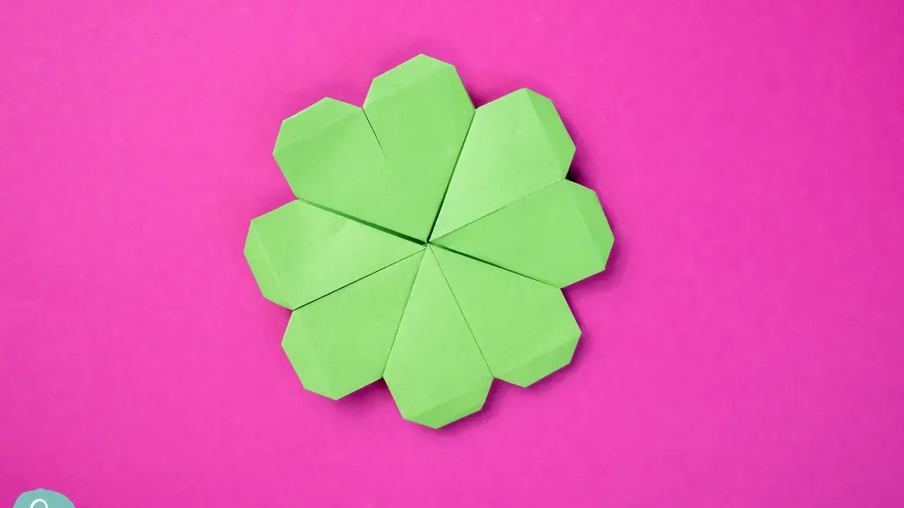 Ein grüner Origami-Glücksbringer, der wie ein Kleeblatt aussieht, auf einem pinken Hintergrund.