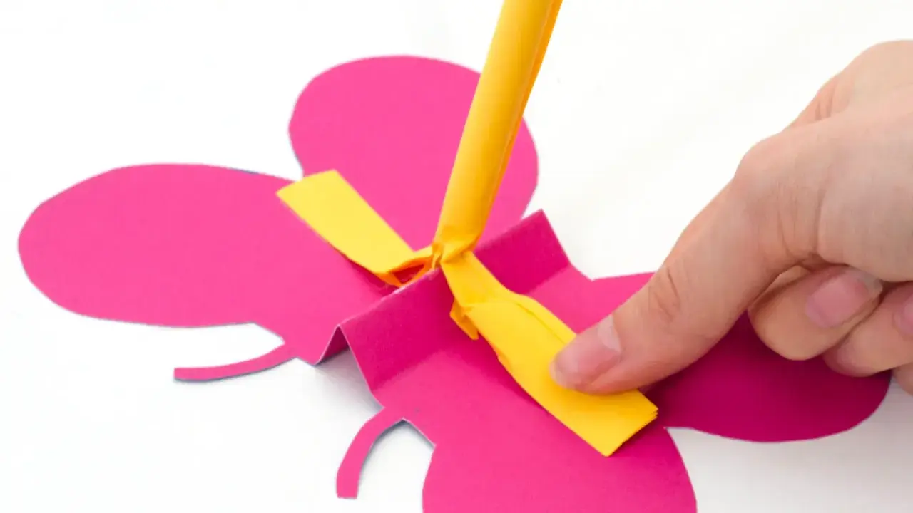 Hand bastelt fliegende Schmetterlinge aus pinkem Papier. Ein gelber Streifen wird befestigt.