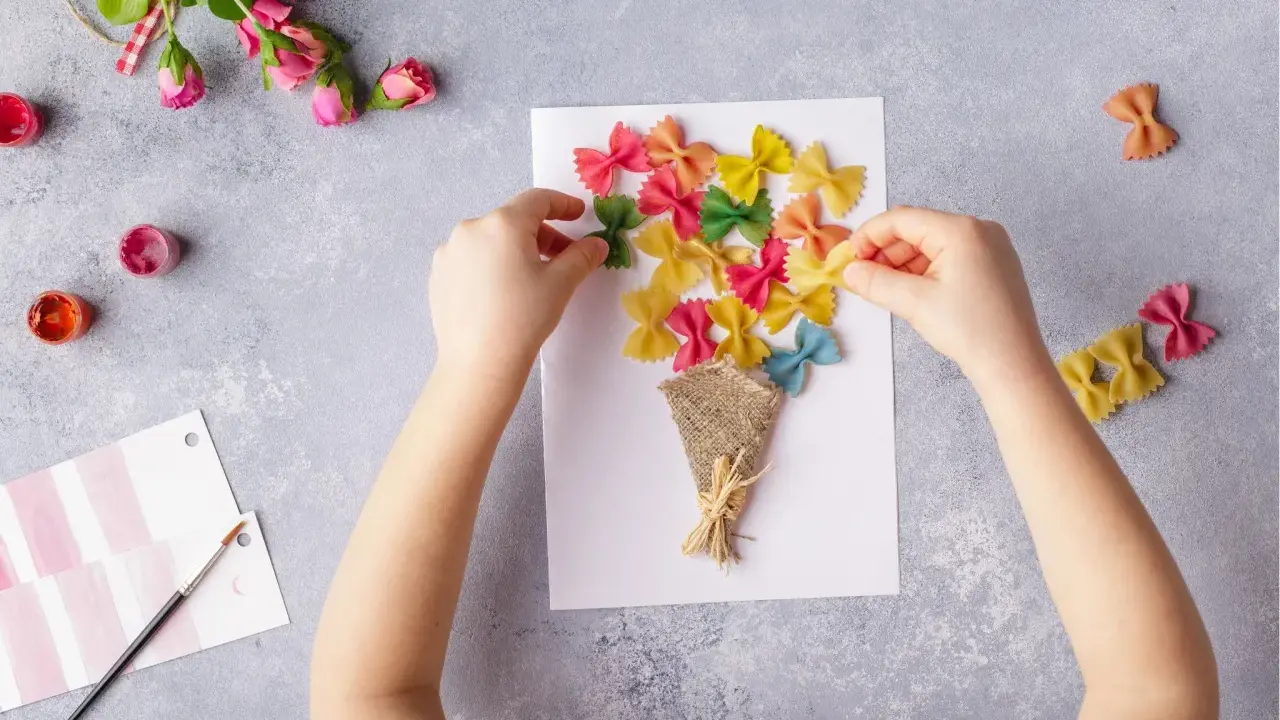 Kinder basteln eine bunte Geburtstagskarte mit farbiger Pasta als Blumenstrauß.