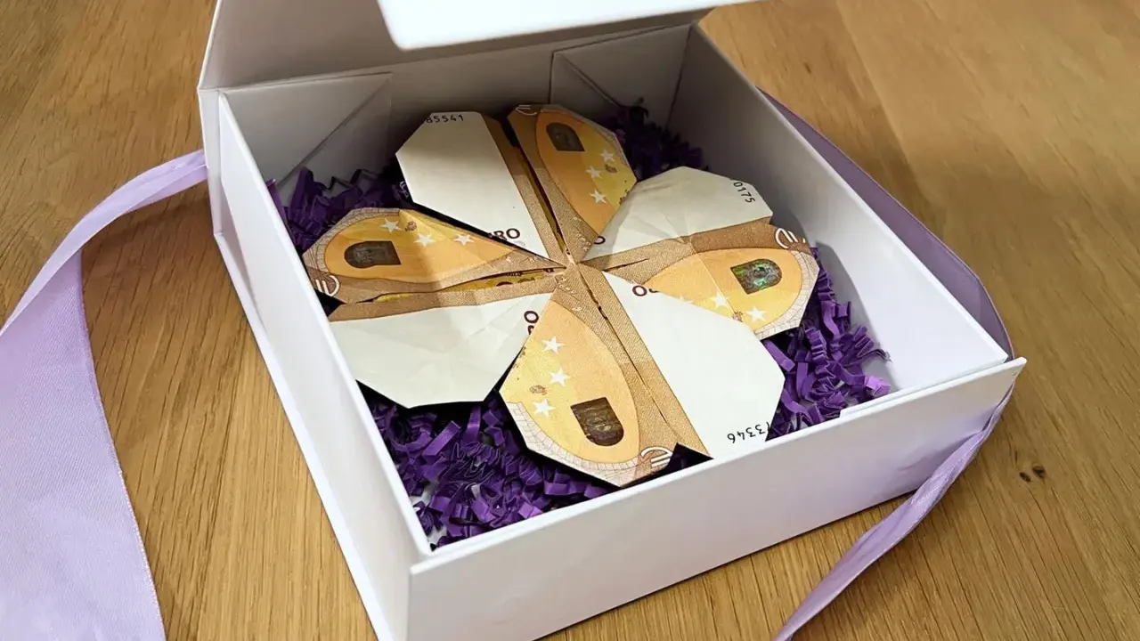 Ein Geschenk: Geld falten blatt in Form eines Kleeblatts, liebevoll in einer weißen Schachtel mit lila Füllung und Band arrangiert.