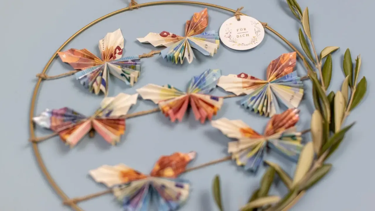 Kreative Deko: Viele bunte Schmetterlinge, gefaltet aus Geld, hängen an einem Ring. Ein schönes Geschenk, um Freude zu schenken.