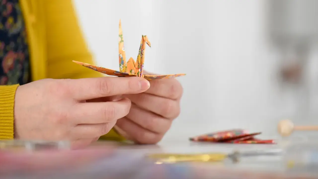 Hände falten einen Kranich aus buntem Papier. Ein schöner Moment während eines Origami Kurses.