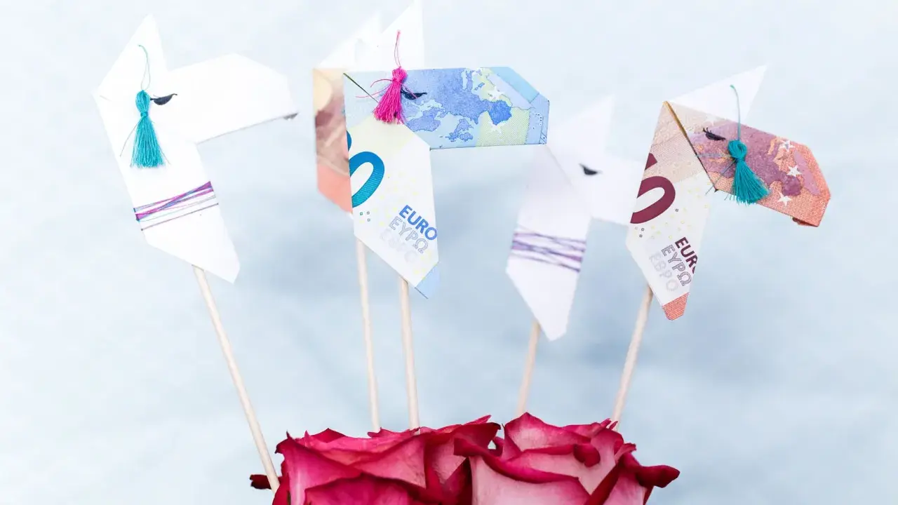 Origami-Pferde aus Geld gefaltet, mit bunten Quasten und Rosen. Ein kreatives Geldgeschenk.