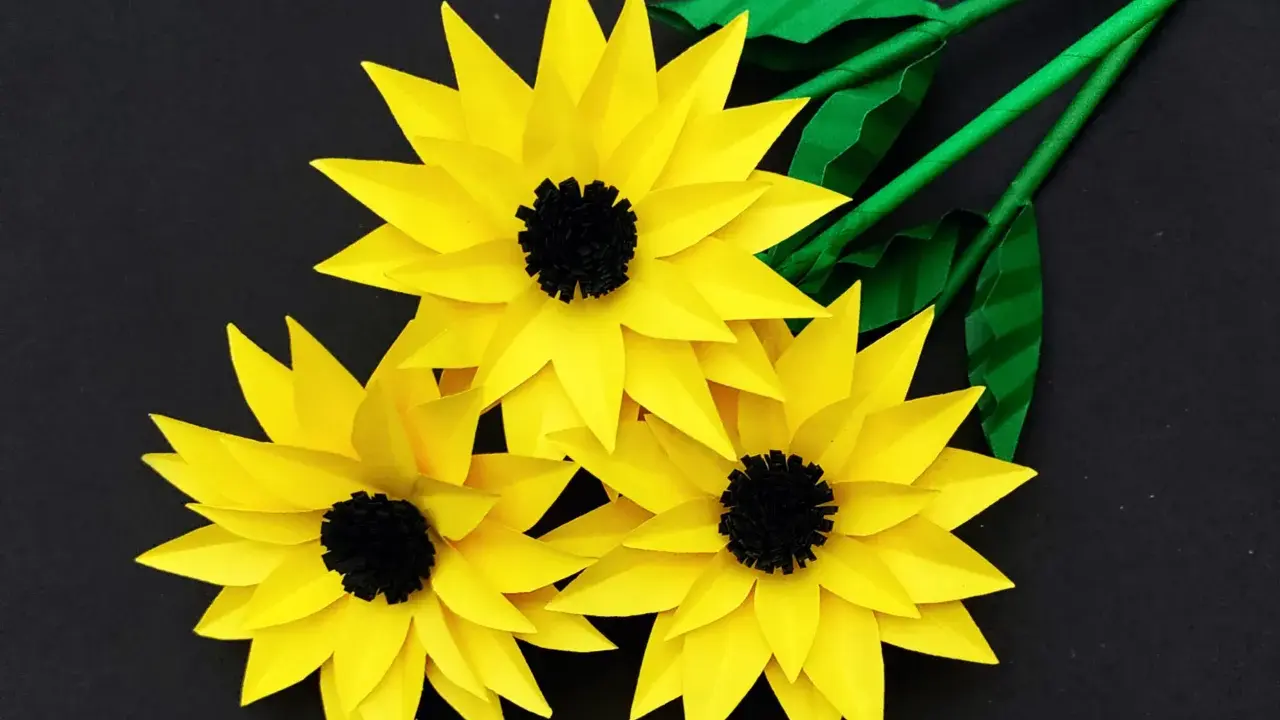 Drei gelbe Papier-Sonnenblumen mit schwarzen Zentren und grünen Stielen, ideal als sonnenblume basteln vorlage.