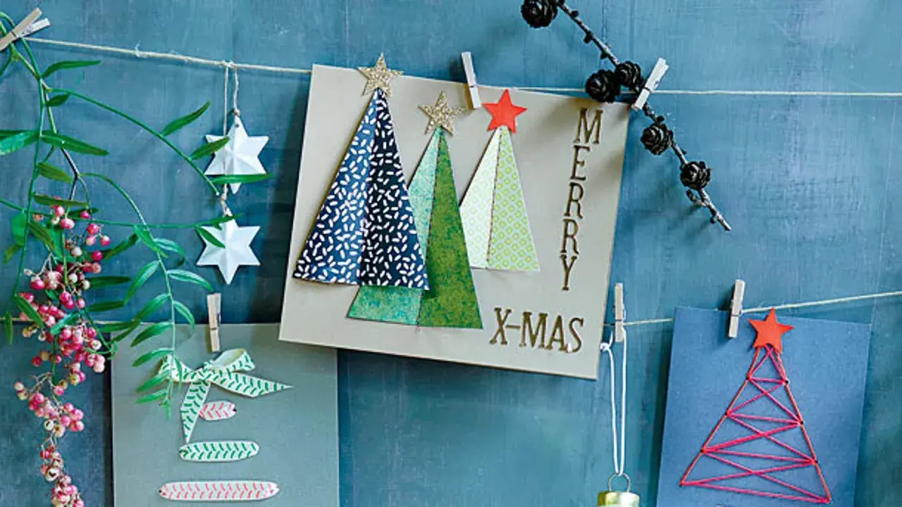Selbstgebastelte Weihnachtskarten mit Bäumen und Sternen hängen an einer Schnur. Ein grüner Zweig mit Beeren und Papiersterne zieren die Szene.