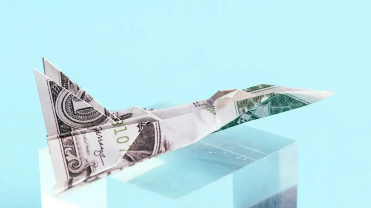 Ein **Flugzeug aus Geld falten** ist ein Kunstwerk. Ein Dollar-Schein wurde zu einem Jet gefaltet, der auf einem transparenten Block thront.