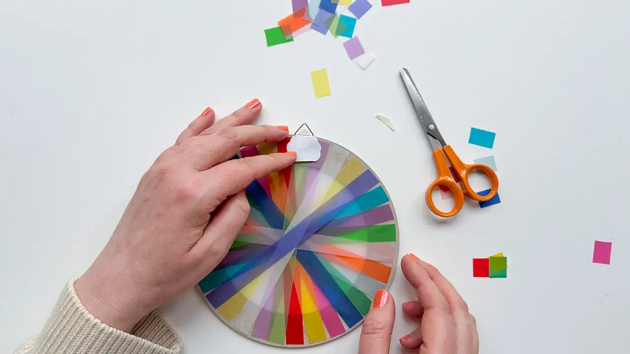 Hände basteln mit transparentsterne falten, bunte Streifen auf einem Kreis, daneben Schere und Konfetti.