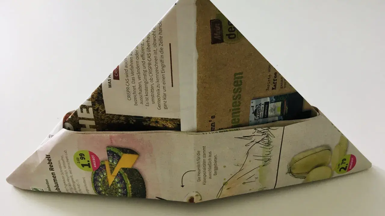 Ein dreieckiger Papierhut, gefaltet aus Zeitungspapier mit Werbung für Käse und Kaffee. Das Papierhut falten ist eine einfache Bastelidee.