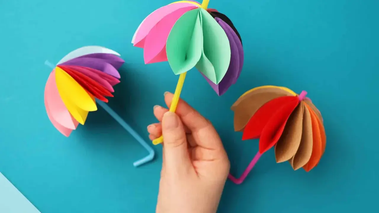 Bunte Papier-Regenschirme, tolle bastelideen einfach und schnell für Kinder. Ein gelber Schirm wird von einer Hand gehalten.