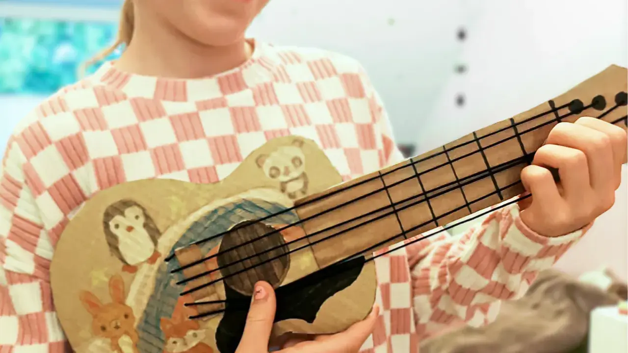 Kind bastelt Gitarre nach Vorlage. Die selbstgemachte Gitarre ist mit süßen Tieren wie Pinguin, Panda, Hase und Fuchs bemalt.