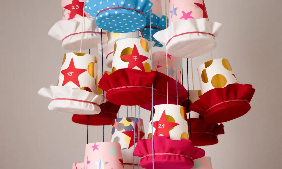 Bunte Becher mit Sternen und Punkten, die als Adventskalender becher basteln dienen. Jede Tasse hat eine Zahl und eine Stoffkappe.