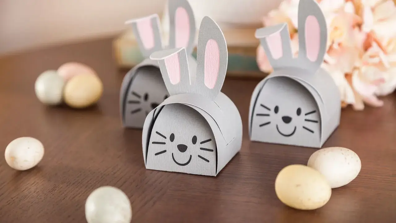 DIY Osternest: Süße Papierhasen mit rosa Ohren und Schokoladeneiern auf Holztisch.