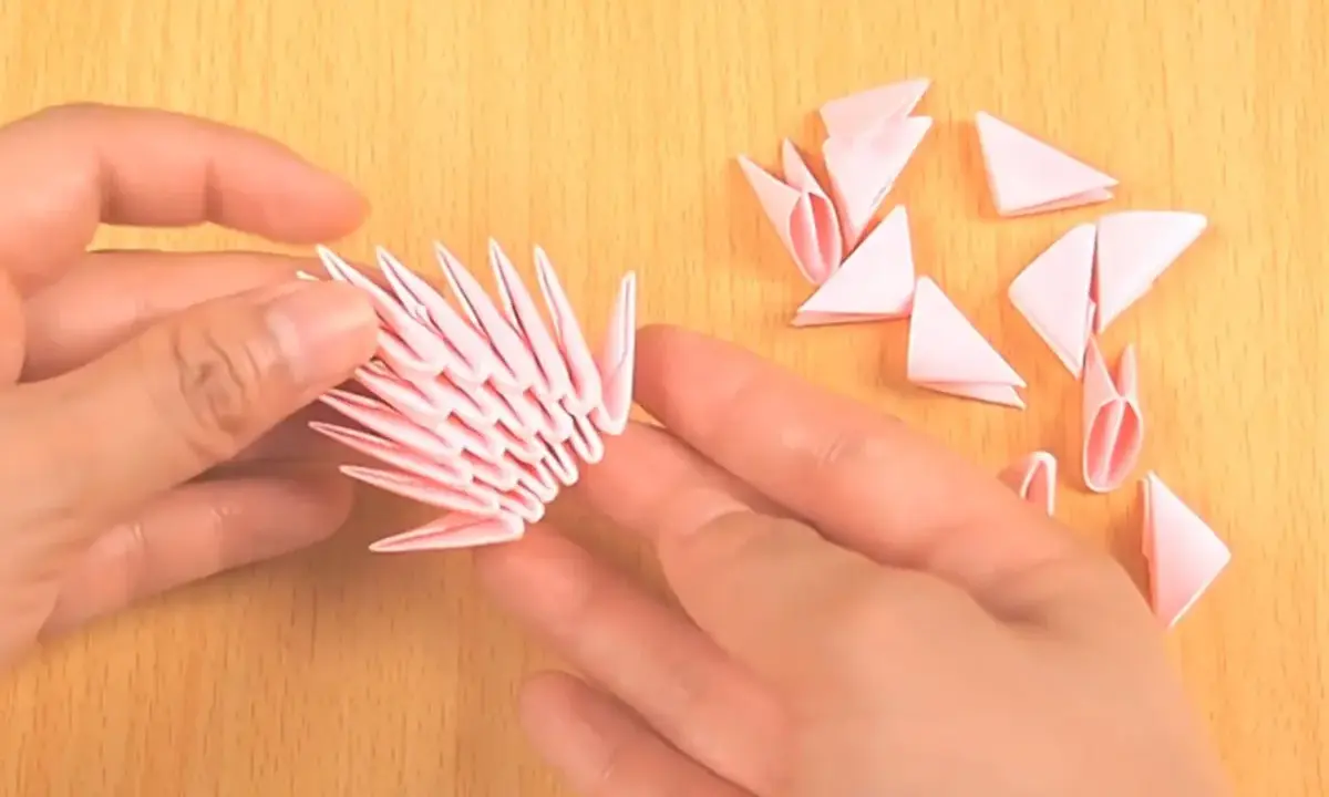 Hände bauen mit rosa Papierstücken ein 3D-Origami-Tier. Die Anleitung ist leicht verständlich.