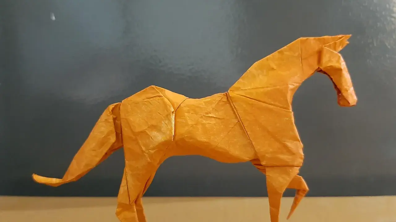 Ein orangefarbenes Origami-Pferd steht auf einem Tisch.