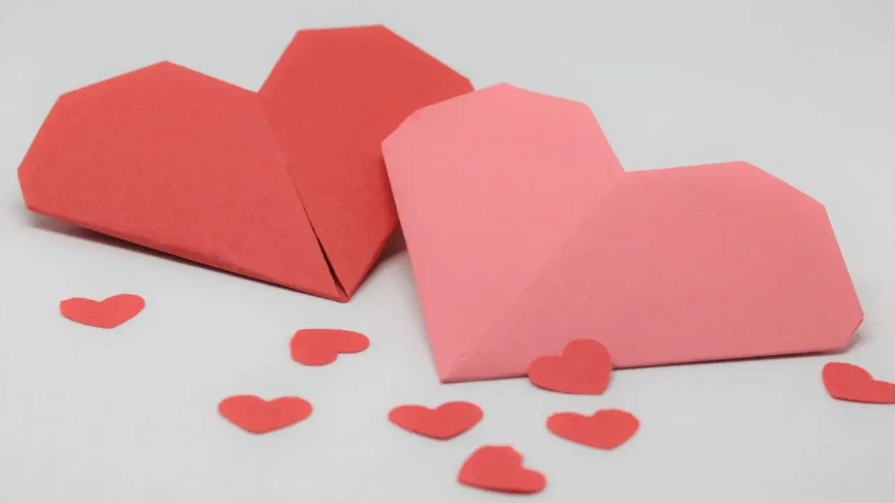 Zwei Origami-Herzen, rot und rosa, umgeben von kleinen roten Herzen. Perfekt zum **Herzen basteln** für den Valentinstag.