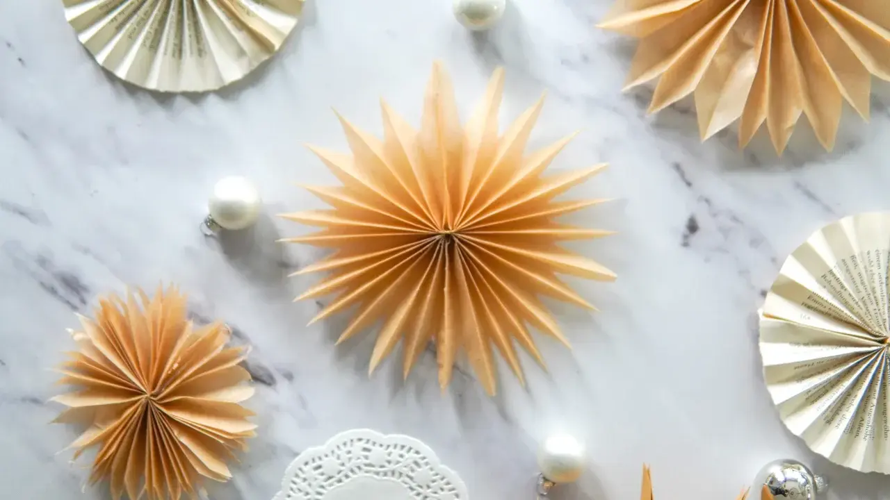 Fächersterne aus Papier, wie bei einer Teebeutel falten Anleitung, schmücken den Marmortisch neben Weihnachtskugeln.