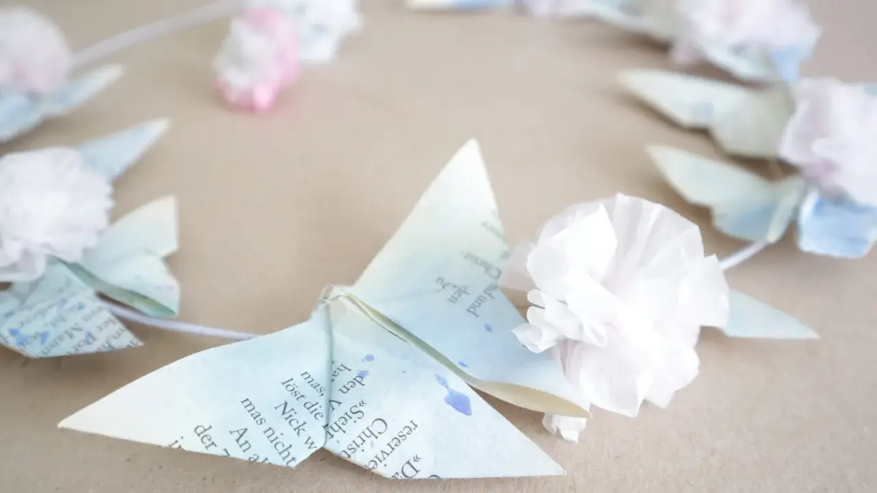 Zarte Origami-Schmetterlinge aus Buchseiten, verziert mit Tupfen und kleinen Papierblumen, bilden einen Kranz. Ein Hauch von origami frühling.