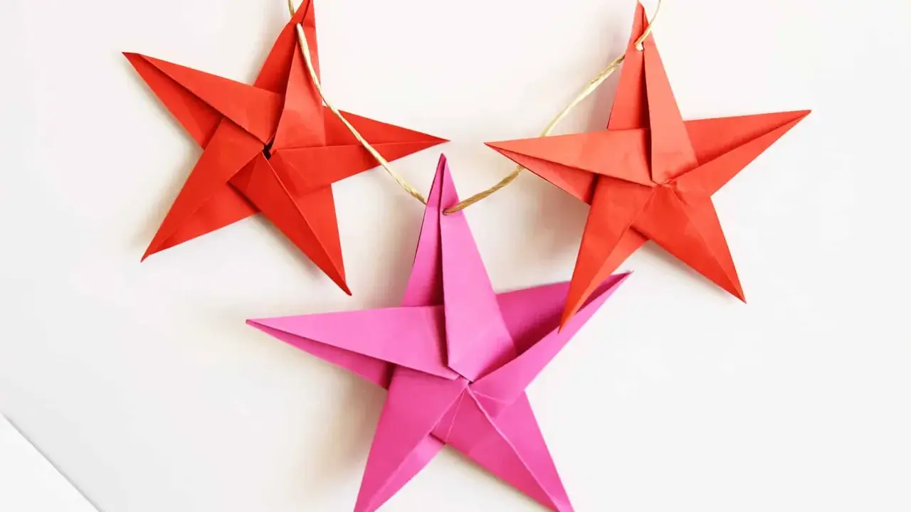 Drei bunte Sterne Origami hängen an einer Schnur. Rote Sterne und ein pinker Stern, perfekt für Weihnachtsdekoration.