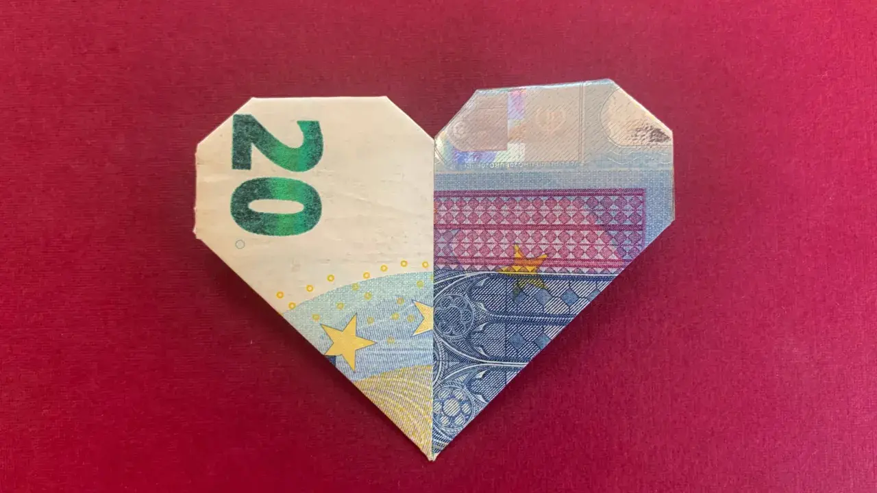 Ein gefaltetes Herz aus 20-Euro-Scheinen auf rotem Untergrund.