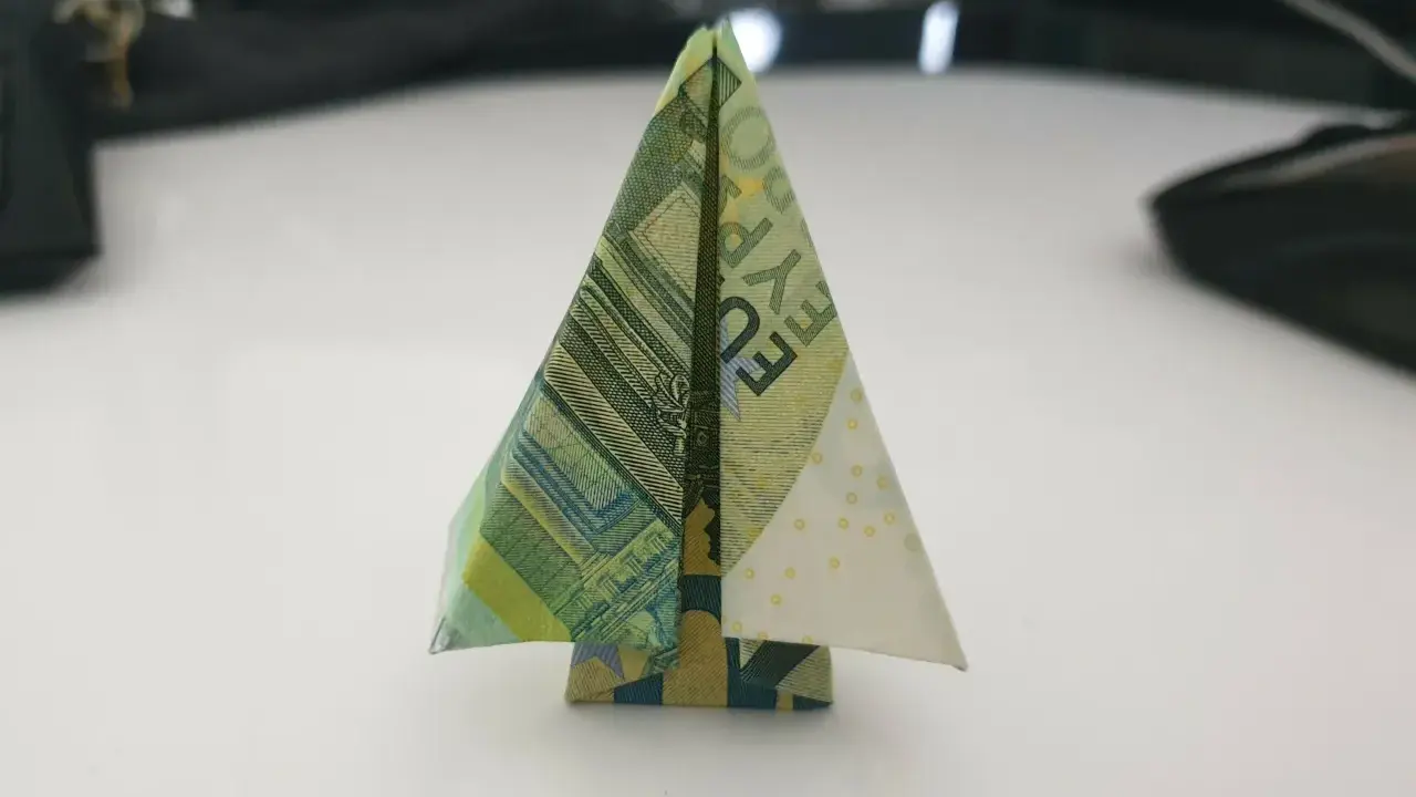 Ein kleiner, gefalteter Baum aus Geldscheinen steht auf einem Tisch. Ein kreativer geld falten baum.