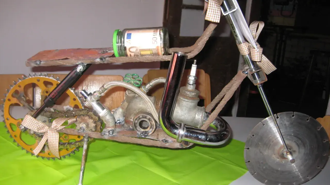 Kreatives Motorrad aus Altmetall, mit einem 50-Euro-Geldschein im Glas als Tank und einem kleinen Motorradhelm-Anhänger.