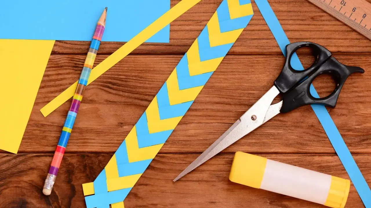 Bunte Streifen aus Papier werden zu einem Lesezeichen gebastelt. Schere, Klebestift und ein farbiger Bleistift liegen bereit.