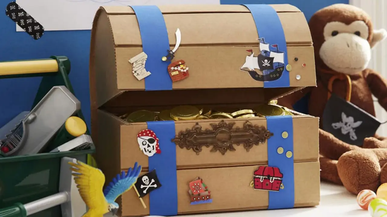 Bastelidee: Eine Schatztruhe aus Pappe, verziert mit Piratenmotiven und gefüllt mit Goldmünzen. Ein Affe hält eine Piratenflagge.