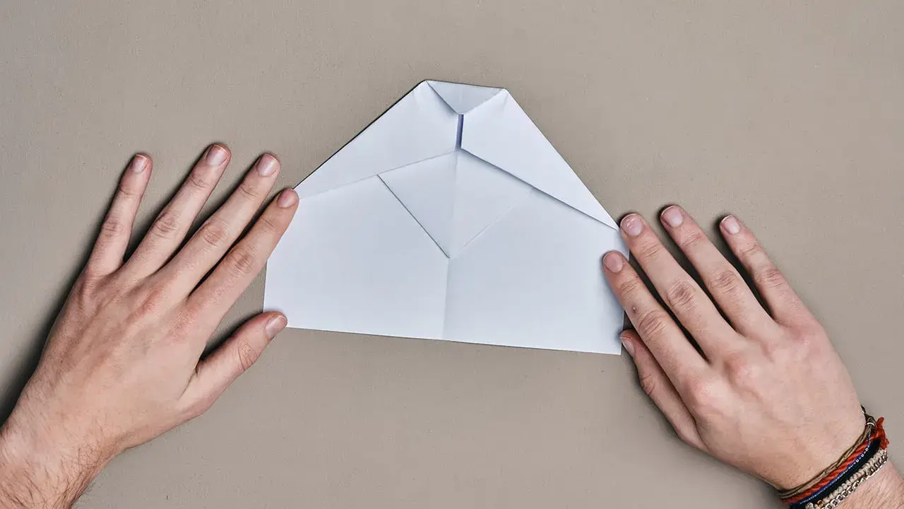 Hände falten einen weißen Papierflieger. Der runder Papierflieger nimmt langsam Form an.