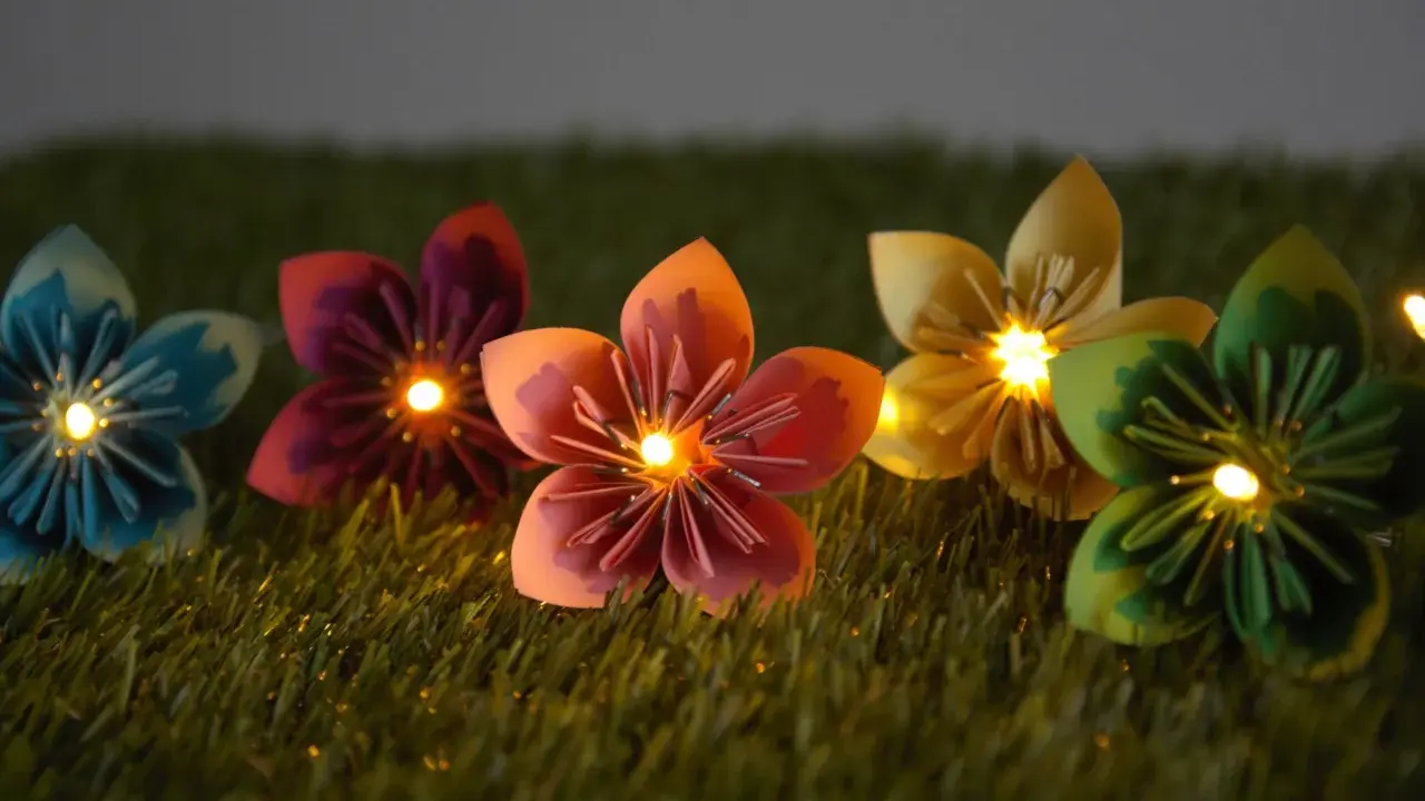 Bunte Papierblumen leuchten auf grünem Gras. Eine selbstgebastelte Lichterkette, die Kinder lieben werden.
