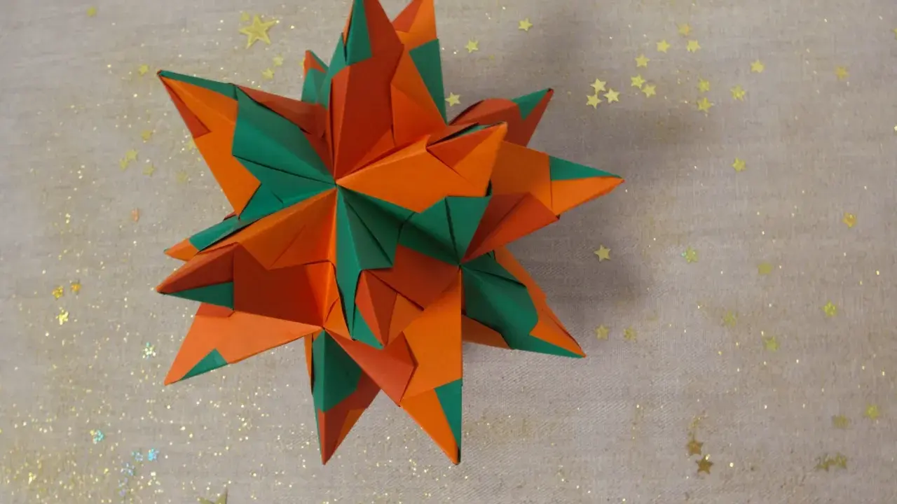 Ein sternförmiges Origami-Objekt in Orange und Grün, das an einen funkelnden Winterhimmel erinnert.