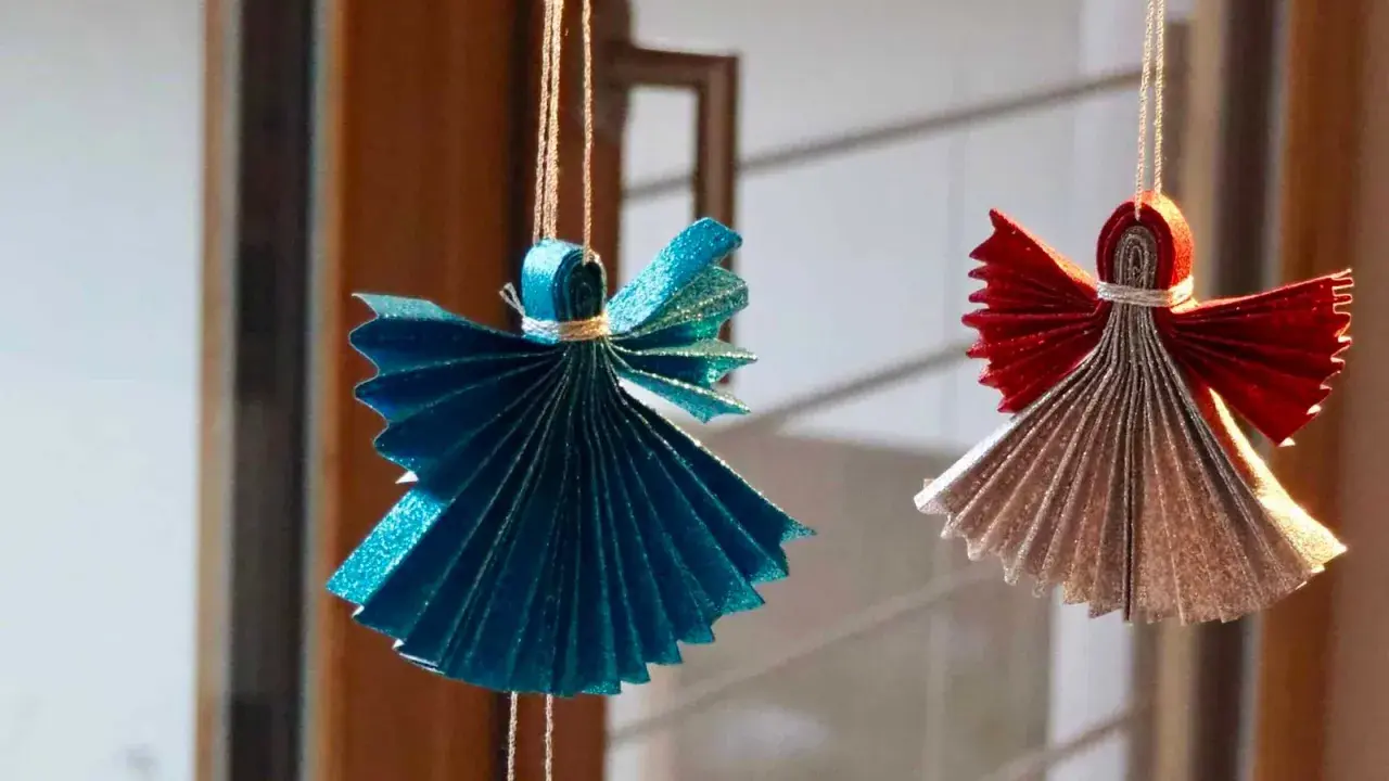 Zwei glitzernde Origami Weihnachts Engel, einer in Blau, der andere in Rot und Silber, hängen an Fäden.