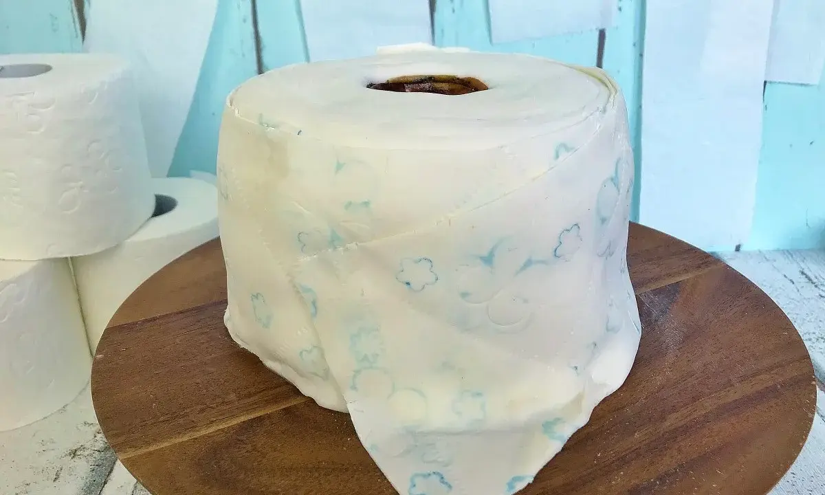 Eine Torte aus Toilettenpapier basteln: Ein realistisch aussehender Kuchen in Form einer Toilettenpapierrolle, verziert mit blauen Blumenmustern.
