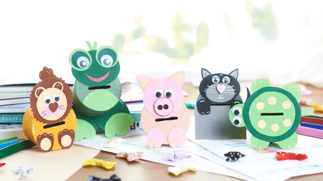 Vier selbstgebastelte Spardosen in Tierform: Löwe, Frosch, Schwein und Katze. Eine Schildkröte steht daneben.