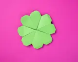 Ein grüner Origami-Glücksbringer, der wie ein Kleeblatt aussieht, auf einem pinken Hintergrund.
