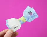 Ein 20-Euro-Schein ist zu einer Schleife gefaltet. Ein Finger hält das gefaltete Geld.