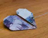 Ein Herz aus gefalteten Geldscheinen liegt auf Holz. Die Noten zeigen die Zahl 20.