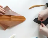 Zwei Hände falten Papier, eine an einem komplexen braunen Origami, die andere an einem schwarzen. Eine schwierige Origami-Anleitung wird befolgt.