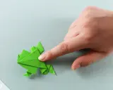 Grüner Origami-Frosch wird von einer Hand geformt. Eine einfache origami vorlage zum Nachfalten.
