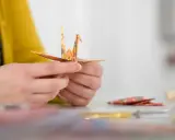 Hände falten einen Kranich aus buntem Papier. Ein schöner Moment während eines Origami Kurses.