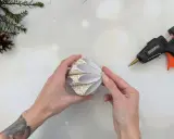 Hände basteln mit Klebepistole und Papier einen schönen DIY Christbaumschmuck. Tannenzweige und Orangenscheiben liegen bereit.