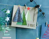 Selbstgebastelte Weihnachtskarten mit Bäumen und Sternen hängen an einer Schnur. Ein grüner Zweig mit Beeren und Papiersterne zieren die Szene.
