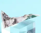 Ein **Flugzeug aus Geld falten** ist ein Kunstwerk. Ein Dollar-Schein wurde zu einem Jet gefaltet, der auf einem transparenten Block thront.
