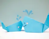 Zwei niedliche Origami-Wale, die Wasser spritzen.
