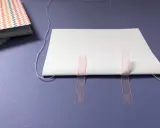 Beim Buch basteln werden weiße Blätter mit rosa Bändern und Faden zusammengefügt.
