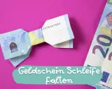 Eine Fliege aus Geld falten ist eine kreative Idee für Geschenke. Hier siehst du eine gefaltete Geld-Fliege auf pinkem Hintergrund.