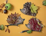 Drei Igel-Bastelvorlagen aus Papier mit Blättern, Garn und Ästen. Ein Igel hat braunes Garn, ein anderer Herbstblätter, der dritte ist mit roten Garn verziert.