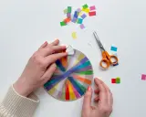 Hände basteln mit transparentsterne falten, bunte Streifen auf einem Kreis, daneben Schere und Konfetti.