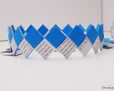 Eine blaue und weiße Papierkrone, die aus gefalteten Papierstreifen gefertigt wurde. Die Streifen sind mit Text bedruckt, was die Krone zu einem besonderen Kunstwerk macht.