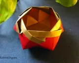 Eine kunstvolle origami schale in Rot und Gold, daneben ein grünes Blatt.