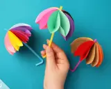 Bunte Regenschirme aus Tonpapier, perfekt zum Basteln mit Kindern. Ein gelber Schirm wird von einer Hand gehalten.